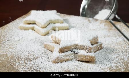 Biscotti fatti in casa a forma di stella, stratificati e appena in polvere, poggiano su una superficie di legno. Lo zucchero in polvere viene setacciato sopra di loro. Foto Stock