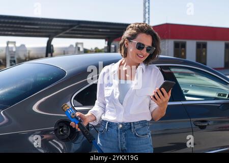 Donna tiene un ugello di alimentazione dell'idrogeno su una stazione di rifornimento dell'idrogeno. Rifornimento di carburante per auto con idrogeno. Foto Stock