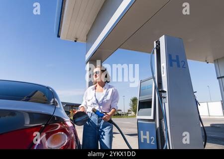 Donna tiene un ugello di alimentazione dell'idrogeno su una stazione di rifornimento dell'idrogeno. Rifornimento di carburante per auto con idrogeno. Foto Stock