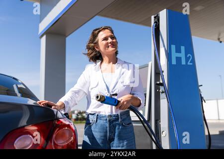 Donna tiene un ugello di alimentazione dell'idrogeno su una stazione di rifornimento dell'idrogeno. Rifornimento di carburante per auto con idrogeno. Foto Stock