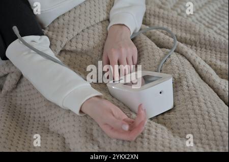 Donna che misura la pressione sanguigna con un tonometro a letto Foto Stock