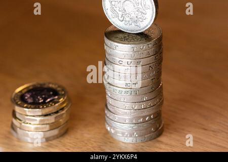 Una singola moneta britannica da una sterlina salta precariamente in cima a un alto mucchio di monete simili. Una pila più piccola di monete da un libbre si trova a sinistra, su un li Foto Stock