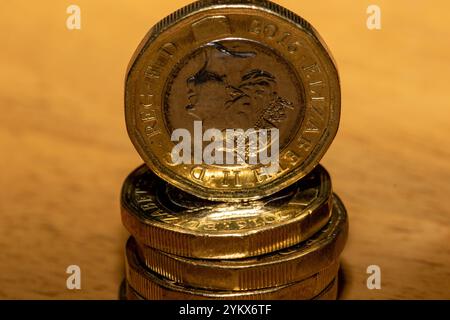 Primo piano di una pila di monete inglesi da un libbra su una superficie di legno marrone chiaro. La moneta superiore è chiaramente visibile, mostrando il profil della regina Elisabetta II Foto Stock