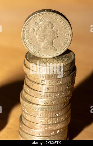 Una pila di monete inglesi da una sterlina, con una sola moneta bilanciata. Le monete sono color oro e mostrano il profilo della regina Elisabetta II. Il backgro Foto Stock