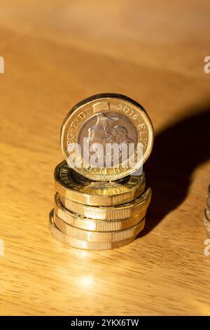 Uno scatto ravvicinato di una pila di monete inglesi da un libbra su una superficie di legno marrone chiaro. La moneta principale è un numero di 2016, che mostra il pro della regina Elisabetta II Foto Stock