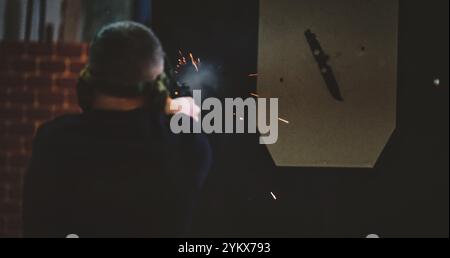 L'immagine raffigura un uomo a un raggio di tiro. L'uomo viene visto da dietro e sta sparando con una pistola, con scintille visibili e fumo proveniente dalla pistola. Foto Stock