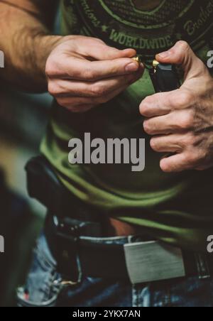 Uomo che sta caricando proiettili in una rivista, che probabilmente appartiene ad un'arma da fuoco. indossa un abbigliamento casual, tra cui una camicia verde e jeans. C'è anche un Foto Stock