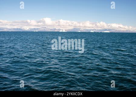 Le acque aperte si estendono attraverso la baia di Disko in Groenlandia, punteggiate di iceberg alla deriva. In lontananza, la sagoma aspra dell'isola di Disko si erge contro Foto Stock