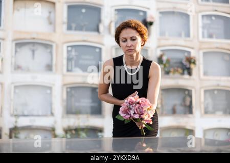 Donna addolorata in nero che mette il bouquet sulla tomba Foto Stock