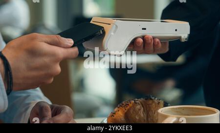 Primo piano, il visitatore paga la bolletta dell'ordine del cibo nel bar ristorante un cameriere irriconoscibile che tiene in mano la scansione wi-fi del terminale utilizzando la tecnologia NFC senza contatto dello smartphone Foto Stock