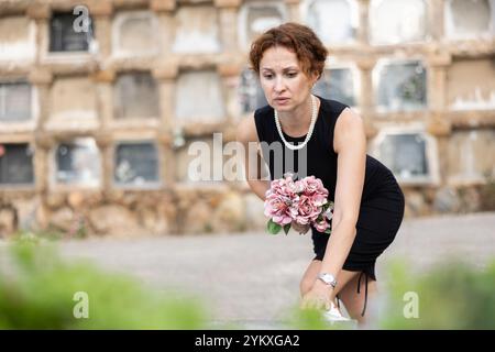 Donna addolorata in nero che mette il bouquet sulla tomba Foto Stock