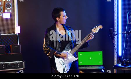 Artista rock donna che suona il basso accanto al display mockup sul dispositivo, facendo un'esibizione di musica dal vivo sul palco del nightclub. Artista che si comporta alla moda e ribelle con uno stile audace. Telecamera A.. Foto Stock