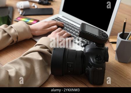 Le mani di una fotografa con un computer portatile moderno e una fotocamera su un tavolo in legno, primo piano Foto Stock