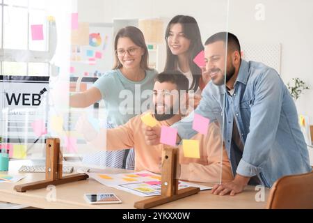 Un team di designer che infila appunti di carta su vetro in ufficio Foto Stock