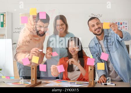 Un team di designer che infila appunti di carta su vetro in ufficio Foto Stock