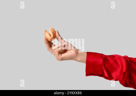 Mano femminile che tiene biscotti della fortuna su sfondo grigio, primo piano Foto Stock