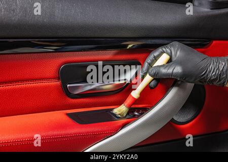 Un addetto all'autolavaggio pulisce con cura l'interno di un'auto di lusso con una spazzola e una pulizia dettagliata in primo piano. Spazzolare via la polvere dall'interno dell'auto Foto Stock