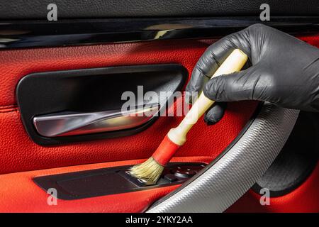 Un addetto all'autolavaggio pulisce con cura l'interno di un'auto di lusso con una spazzola e una pulizia dettagliata in primo piano. Spazzolare via la polvere dall'interno dell'auto Foto Stock