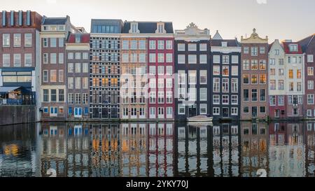 Mentre il sole tramonta su Amsterdam, gli affascinanti canali riflettono la splendida architettura di edifici storici adornati con colori autunnali, creando un'atmosfera serena e pittoresca. Foto Stock