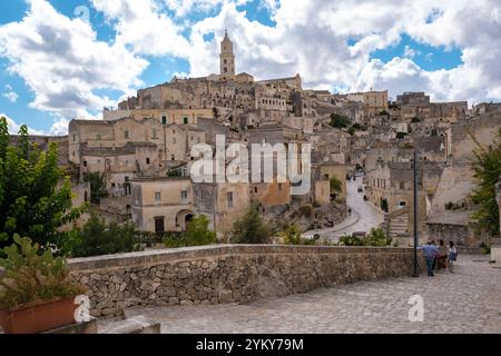 Passeggiando attraverso gli storici sentieri acciottolati di Matera, i visitatori si meravigliano davanti alla splendida architettura scolpita nella pietra, sotto uno sfondo di Foto Stock