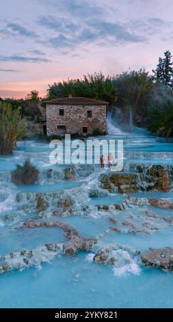 I visitatori possono godersi le calde acque terapeutiche delle terme di Saturnia mentre il sole tramonta, illuminando il paesaggio naturale, gli storici edifici in pietra, e Foto Stock