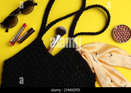 Composizione piatta con sacchetto per la spesa in macrame e prodotti per il trucco su sfondo giallo Foto Stock