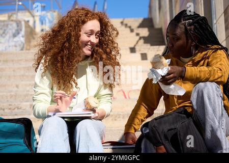 Studenti sorridenti che chiacchierano e mangiavano sulle scale all'aperto Foto Stock
