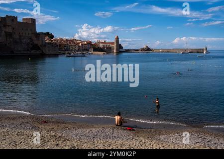 Vista sul mare della città di Collioure con il castello reale e il faro della chiesa di Notre-Dame-des-Anges e la spiaggia dove le famiglie nuotano Foto Stock