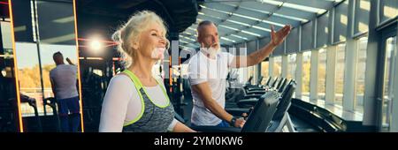 Uomo e donna sorridenti anziani, impegnati in un allenamento tapis roulant in una vivace palestra. Motivazione a rimanere attivi e sani. Foto Stock