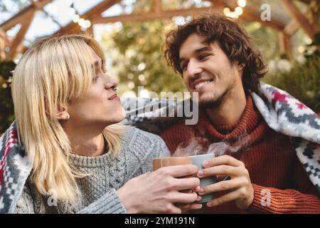 In un ambiente tranquillo all'aperto, due giovani e bellissimi uomini si godono compagnia mentre condividono bevande calde. L'atmosfera intima, impreziosita da un bianco Foto Stock