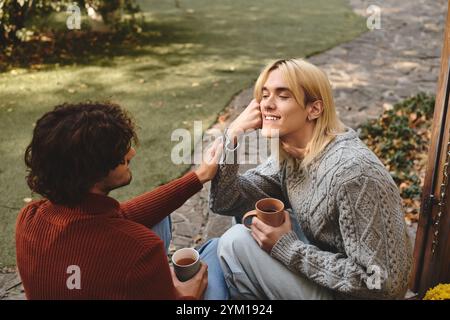 Due bellissimi giovani uomini si divertono a vicenda in compagnia all'aperto sorseggiando bevande calde. Foto Stock