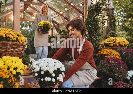 In un bellissimo giardino pieno di fiori colorati, giovani coppie gay si impegnano gioiosamente a coltivare fiori. I loro sorrisi riflettono una passione condivisa Foto Stock