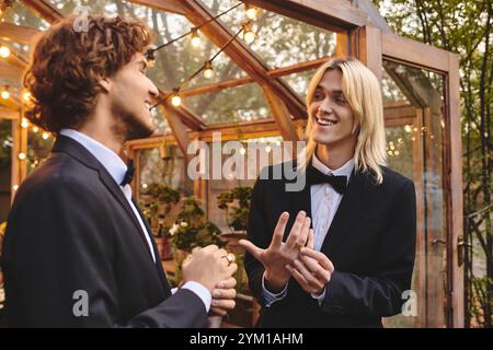 Due giovani e attraenti uomini si impegnano in una discussione animata mentre si vestono con abiti sofisticati in un affascinante giardino. L'atmosfera calda lo e' Foto Stock