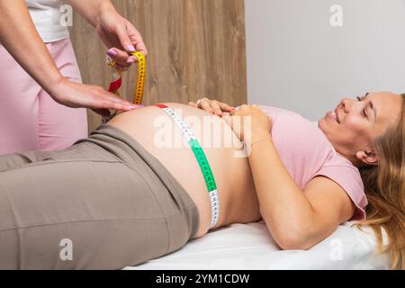 Ginecologo che misura la pancia di una donna incinta con un nastro che esegue il controllo prenatale Foto Stock