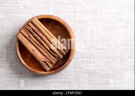 Bastoncini di cannella Ceylon in una ciotola di legno su lino, con spazio vuoto per il testo. Strisce di corteccia intere e secche disposte parallelamente di Cinnamomum verum. Foto Stock