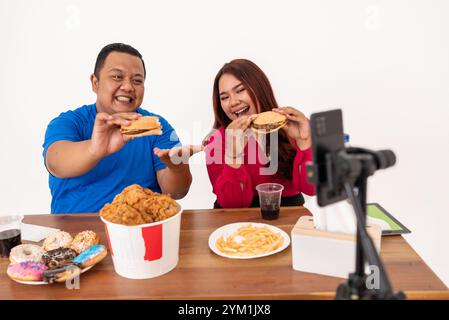 I vlogger del cibo si godono deliziosamente un banchetto di fast food con la fotocamera, festeggiando insieme Foto Stock