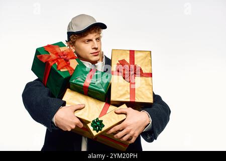 Un uomo alla moda è in piedi con sicurezza mentre tiene in mano una pila di regali splendidamente avvolti in colori festosi. Foto Stock