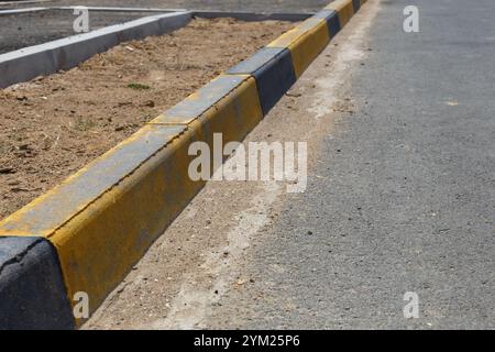 Un cordolo a righe giallo e nero. bordo marciapiede e strada asfaltata Foto Stock