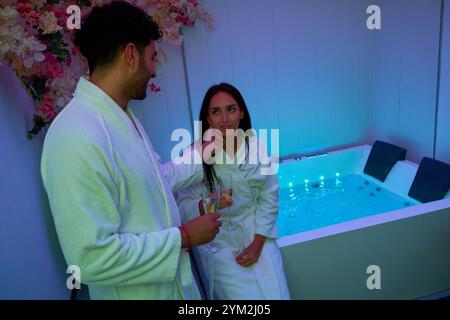 Un uomo e una donna sono in una vasca da bagno, con l'uomo che tiene un bicchiere di vino. La scena è rilassata e intima, in quanto la coppia si diverte a vicenda Foto Stock