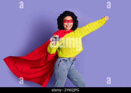 Ritratto fotografico di una bella ragazza con carta di credito che vola supereroina vestito con elegante indumento giallo isolato su sfondo di colore viola Foto Stock