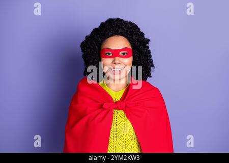 Ritratto fotografico di una giovane donna attraente e allegra supereroina vestita con eleganti abiti gialli isolati su sfondo di colore viola Foto Stock