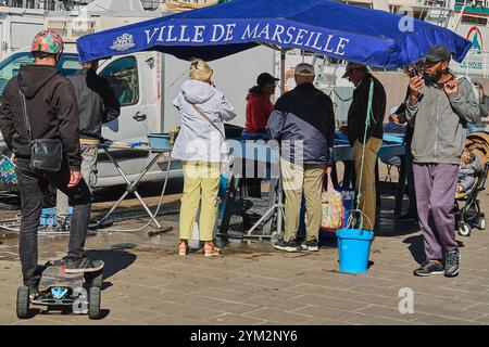 Marsiglia. Francia - 20 novembre 2024: Un venditore di pesce al Porto Vecchio di Marsiglia, che si occupa di pesce fresco al suo banco. Circondato da un edificio storico Foto Stock