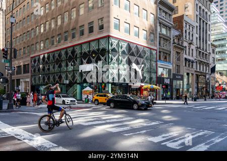 Un uomo con biciclette in attesa al semaforo con il negozio PUMA Flagship sulla 5th Avenue sullo sfondo. Foto Stock