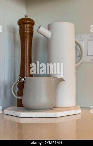 Una caraffa bianca e un macinacaffè in legno sono su un piano di appoggio in marmo. La caraffa è piena d'acqua e il macinacaffè è vuoto. La scena è semplice Foto Stock