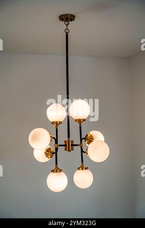 Un grande lampadario con lampadine bianche pende dal soffitto. Il lampadario è realizzato in ottone e ha una catena dorata. La luce del lampadario è bri Foto Stock
