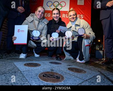 20 novembre 2024, Brandeburgo, Cottbus: I ciclisti Emma Hinze (l-r), Pauline Grabosch e Lea Sophie Friedrich siedono di fronte al municipio di Cottbus mentre ricevono le loro nuove targhe per "la strada della gloria". Gli atleti hanno vinto tutte le medaglie ai Giochi Olimpici di Parigi del 2024. Queste targhe sono state aggiunte a "The Road to Glory" durante un tributo pubblico. Oltre a vincere una medaglia ai Giochi olimpici, l'appartenenza a un club sportivo Cottbus o la nascita a Cottbus è un prerequisito per l'inclusione in "The Path to Glory". Ad oggi, sono stati premiati 76 vincitori delle medaglie olimpiche e paralimpiche Foto Stock