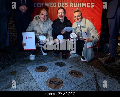20 novembre 2024, Brandeburgo, Cottbus: I ciclisti Emma Hinze (l-r), Pauline Grabosch e Lea Sophie Friedrich siedono di fronte al municipio di Cottbus mentre ricevono le loro nuove targhe per "la strada della gloria". Gli atleti hanno vinto tutte le medaglie ai Giochi Olimpici di Parigi del 2024. Queste targhe sono state aggiunte a "The Road to Glory" durante un tributo pubblico. Oltre a vincere una medaglia ai Giochi olimpici, l'appartenenza a un club sportivo Cottbus o la nascita a Cottbus è un prerequisito per l'inclusione in "The Path to Glory". Ad oggi, sono stati premiati 76 vincitori delle medaglie olimpiche e paralimpiche Foto Stock