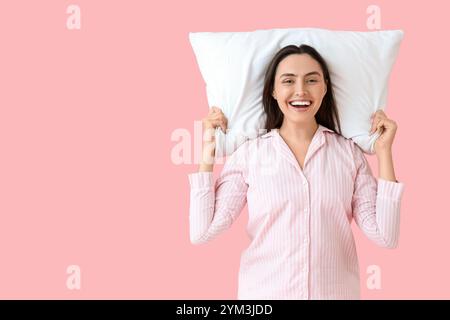 Giovane donna in pigiama a righe con cuscino su sfondo rosa Foto Stock