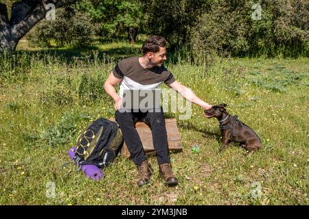 Giovane backpacker che lavora sul suo portatile mentre accarezza il suo cane in modo naturale Foto Stock