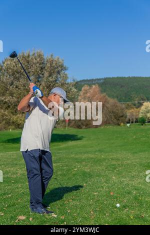 il golfista senior che indossa un berretto e occhiali da sole, colpisce un drive shot sul campo da golf durante un torneo competitivo Foto Stock